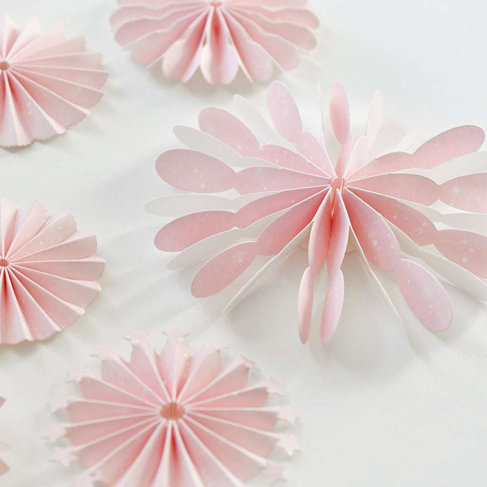 Rosetten aus rosafarbenem Papier, die mit Alexandra Renke Designpapieren und einer Rosette mit Blättern gestanzt wurden, sowie ein floraler Akzent werden elegant auf einem weißen Hintergrund präsentiert.