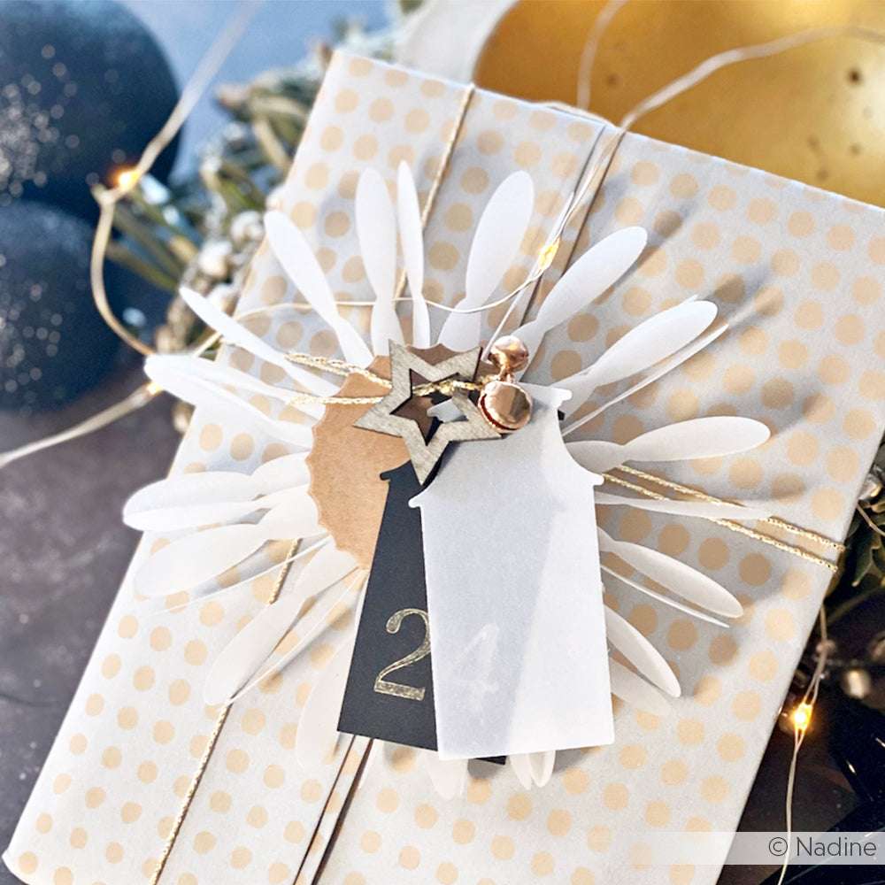 Verpackt in Alexandra Renke Designpapieren mit Polka Dots, verschnürt mit goldener Schnur, Glöckchen, einem Anhänger mit der Aufschrift 24 und verziert mit Papierakzenten sowie einer DieCut Systeme Motivstanze Rosette mit Blättern für einen eleganten Abschluss.
