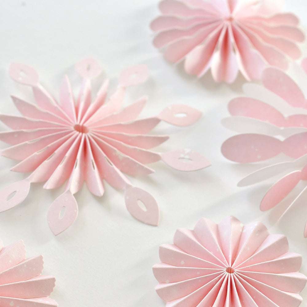 Rosa Papierrosetten und Blumenformen, die mit Alexandra Renke Stanzen für Designpapier hergestellt wurden, sind kunstvoll auf weißem Hintergrund arrangiert.