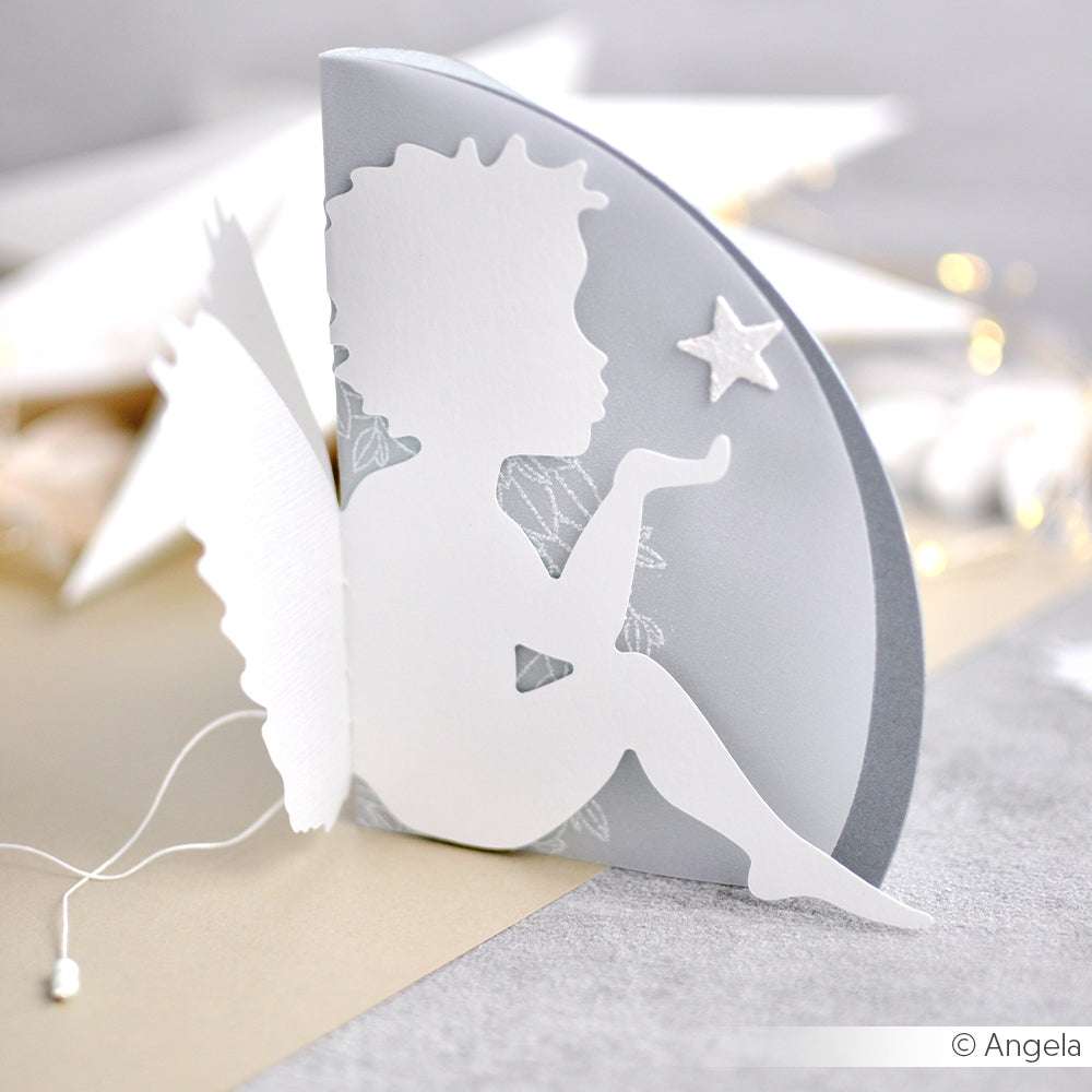 Die weiße Papierfeen-Silhouettenkarte von Alexandra Renke auf grauem Hintergrund mit zarten Flügeln und einem Stern - hergestellt mit Stanzsysteme Dies - eignet sich perfekt als Motivstanze Engel Karte für besondere Anlässe. Seitenansicht gezeigt.