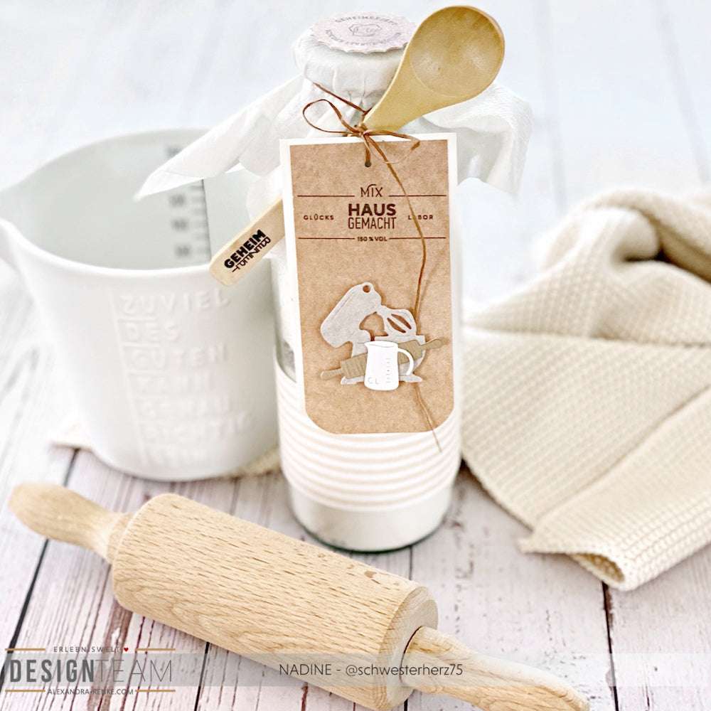 Die Backmischung im Glas von Alexandra Renke wird mit einem Holzlöffel, einem Nudelholz und einem weißen Messbecher geliefert - ideal für müheloses Backen in Kombination mit Ihrem Lieblings-Backhelfer-Set.