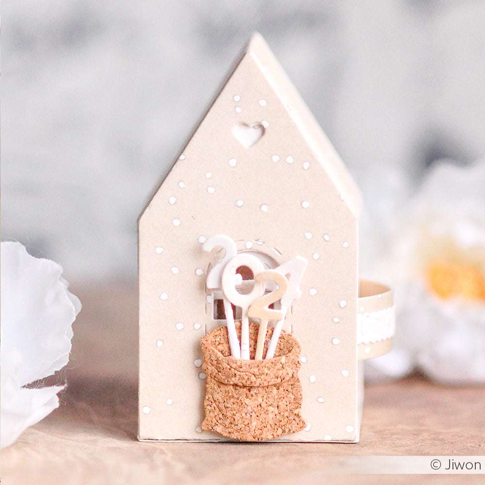 Eine kleine, hausförmige Schachtel von Alexandra Renke enthält "2024"-Sticks in einem Korkbeutel, der mit weißen Punkten verziert ist - ideal zum Kombinieren mit DieCut Systemen oder zum Mischen mit Ihren Lieblingsdesignpapieren für zusätzliches kreatives Flair.