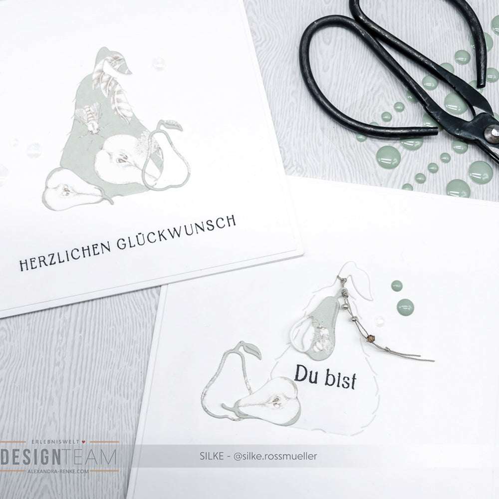 Zwei handgefertigte Karten von Alexandra Renke mit Birnen-Illustrationen, Scheren und grünen gestanzten Verzierungen mit der Motivstanze Abriss Birne, alles auf einer weißen Fläche.