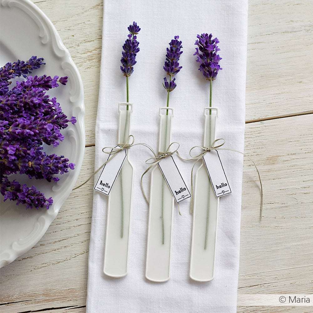 Drei Lavendelzweige in weißen Vasen mit Hallo-Anhängern, hergestellt mit Alexandra Renke Designpapieren und der Motivstanze Lange Flaschenpost, arrangiert auf einer weißen Serviette neben einem Teller.