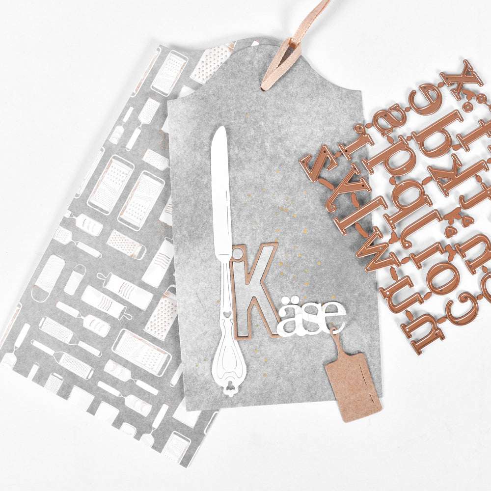 Grauer Geschenkanhänger von Alexandra Renke aus hochwertigem Designpapier, verziert mit einem Käsemesser, dem Schriftzug "Käse" in weißer und kraftvoller Schrift sowie einem kleinen Schneidebrett - ideal für einzigartige Papierprojekte oder Buchbinderei-Akzente.