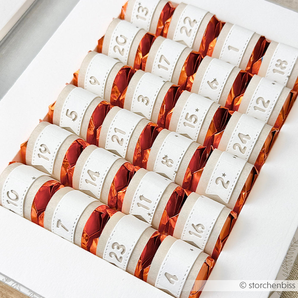Reihen von orangefarbenen Bonbons, die mit weißen Papierbändern von 1 bis 24 beschriftet und in einer Schachtel angeordnet sind - perfekt, um Ihre Lieblings-Alexandra Renke Designpapiere zu präsentieren oder jede Leckerei mit Alexandra Renke DieCut Systemen individuell zu gestalten.