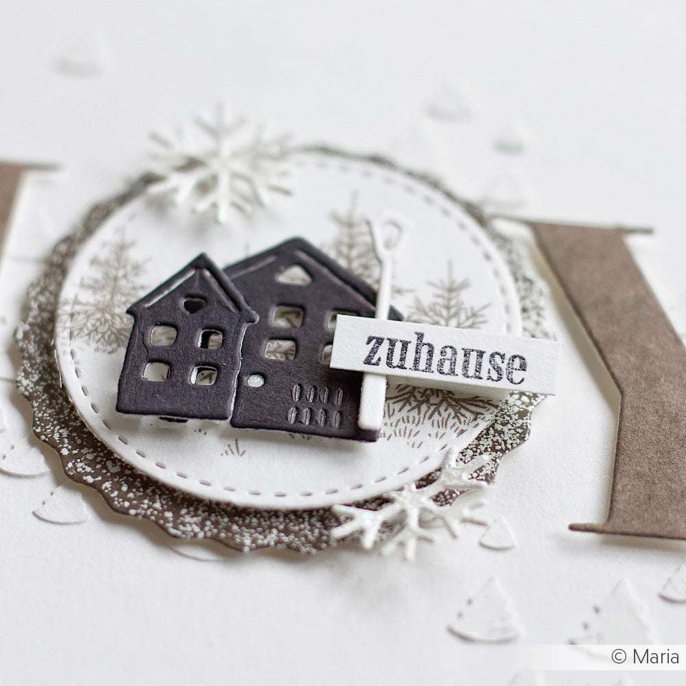 Eine Papierbastelei mit zwei schwarzen Häusern, hergestellt mit Alexandra Renke Motivstanze Kleine Häuserreihe (100% Stahlstempel), mit einem "Zuhause"-Schild, Schneeflocken und Winterbäumen im Hintergrund.
