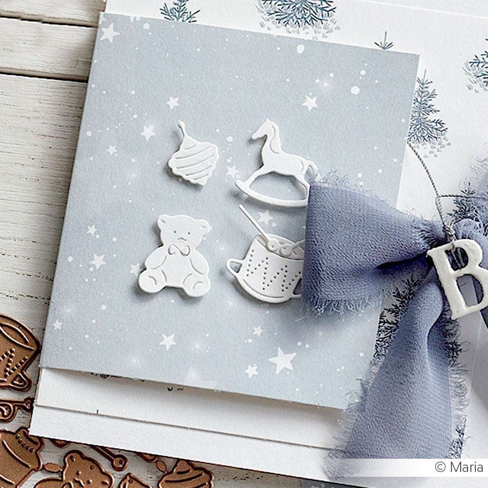 Eine Karte mit weißen Spielzeugformen aus Alexandra Renke Designpapier und einer blauen Schleife auf Sternenhintergrund, verziert mit der Motivstanze Vintage Spielzeug.