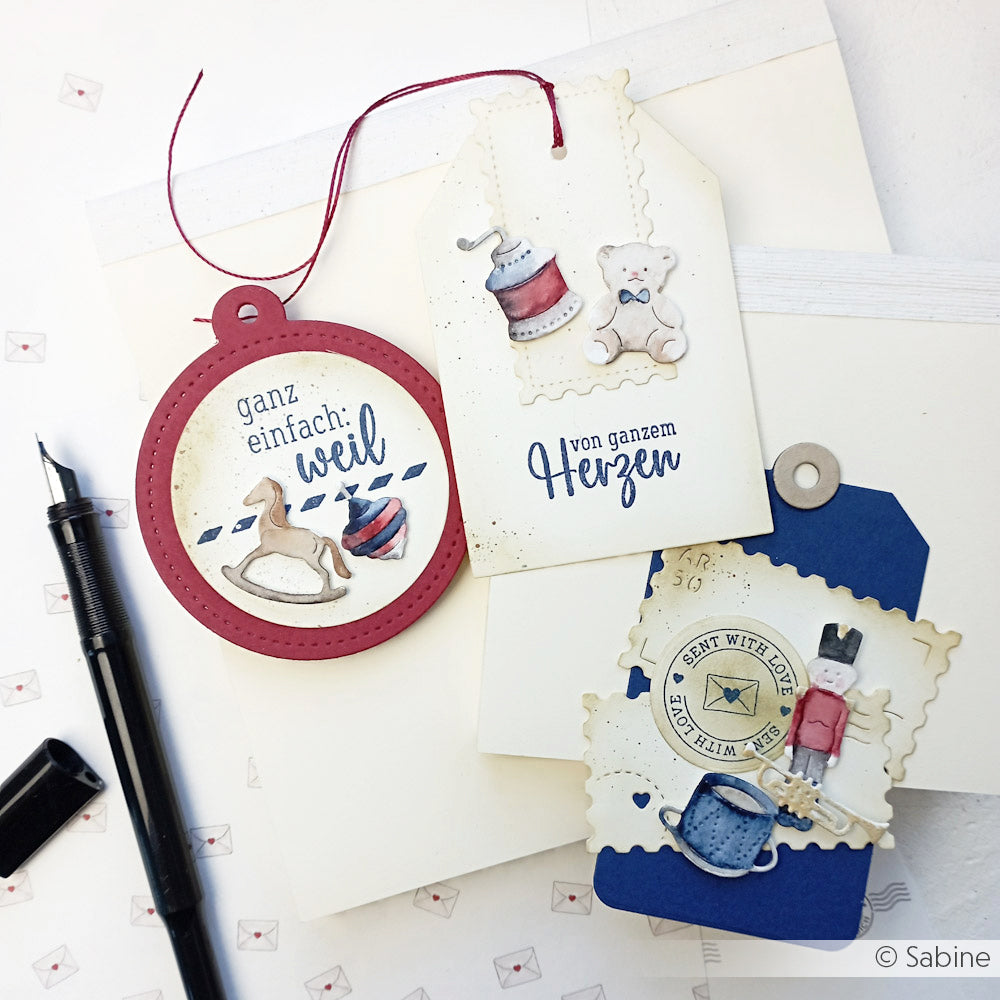 Handgefertigte Geschenkanhänger mit Dekorationen zum Thema Nähen, erstellt mit Alexandra Renke Dies und Motivstanze Vintage Spielzeug, mit deutschem Text, abgebildet neben einem Stift und weißen Umschlägen.