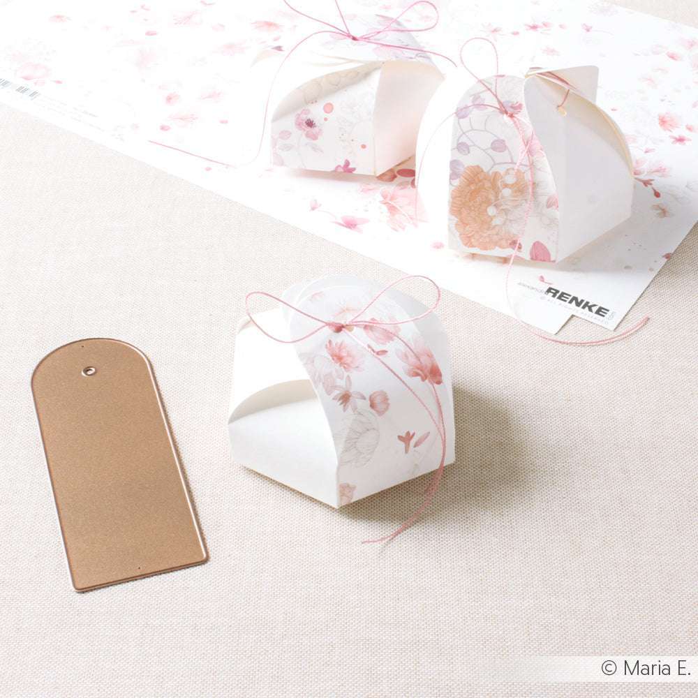 Zwei kleine geblümte Geschenkschachteln mit rosa Schleifenband, daneben ein goldenes Etikett, das mit der Alexandra Renke Big Label Stanze hergestellt wurde. Ideal, um Ihre Lieblingspapiere und Stanzsysteme von Alexandra Renke auf einer hellen Oberfläche hervorzuheben.