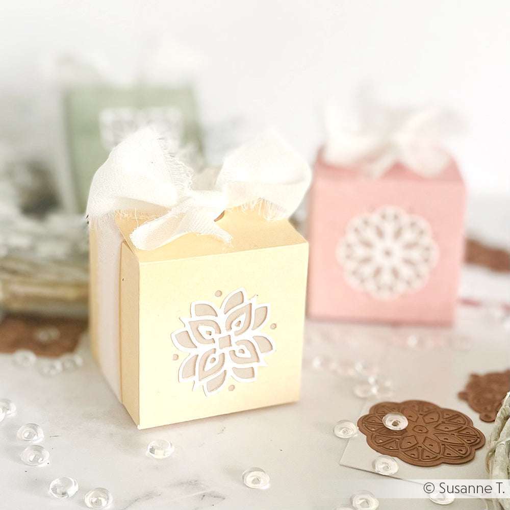 Pastellfarbene Geschenkschachteln mit weißen Schleifen und verschlungenen Blumenausschnitten, hergestellt mit der Motivstanze Ornament von Alexandra Renke, umgeben von Pailletten und Designpapiere-Stanzungen.