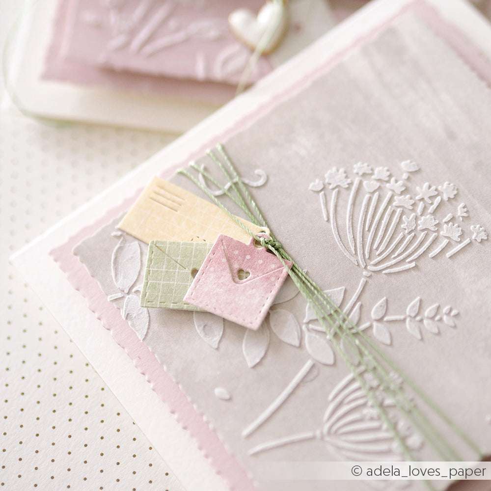 Mit Alexandra Renke Stanzsystemen und Motivstanze geprägte Blumenkarte, gepaart mit pastellfarbenen, mit grüner Schnur gebundenen Umschlägen auf hellem Hintergrund - eine echte Briefe von Herzen-Kreation.
