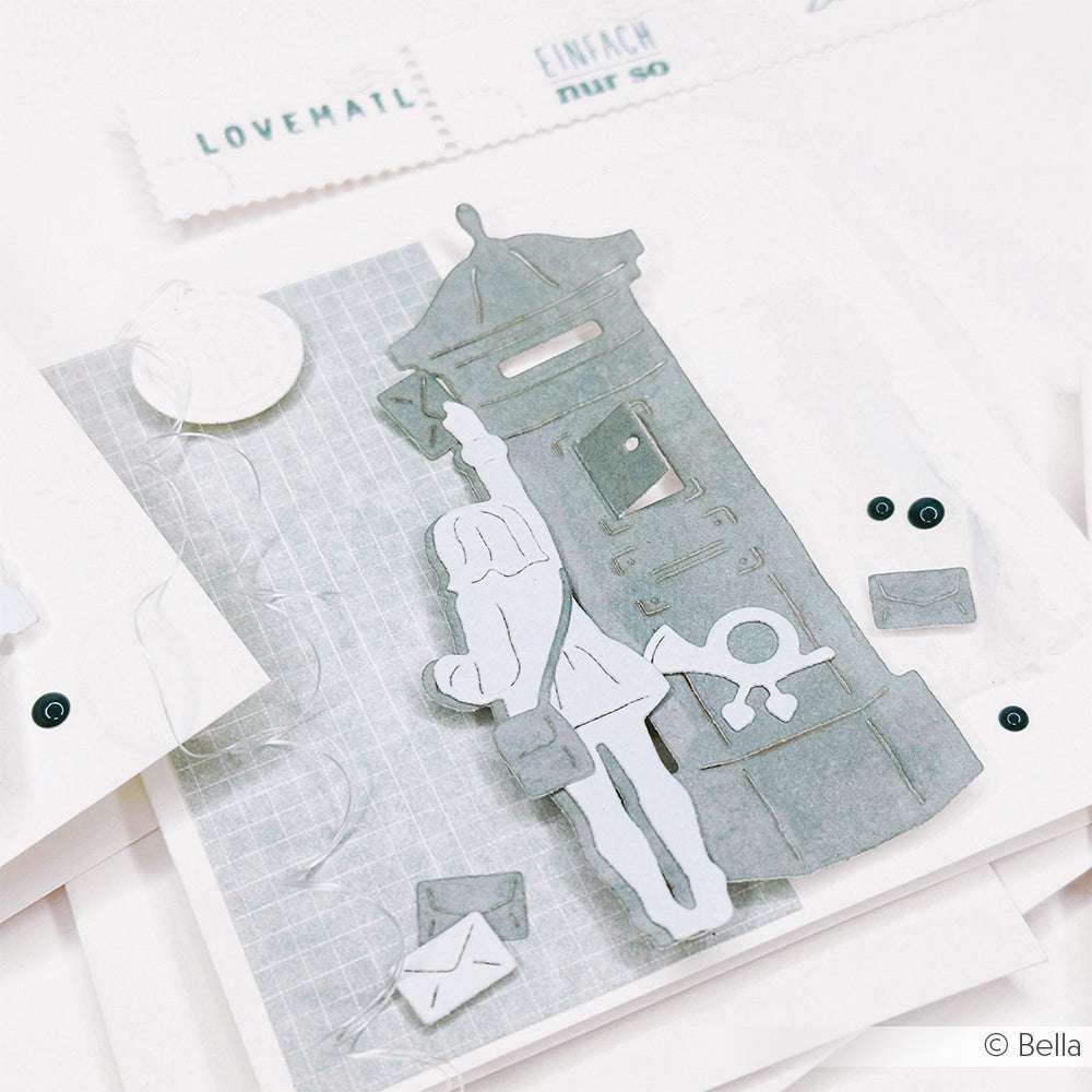 Handgemachte Papierkunst von Alexandra Renke: ein Briefträger an einem Briefkasten mit verstreuten Umschlägen, hergestellt mit Stanzsystemen und dem Brieffreundin-Set. Graue und weiße Farbtöne geben dieser Motivstanze einen charmanten Touch.