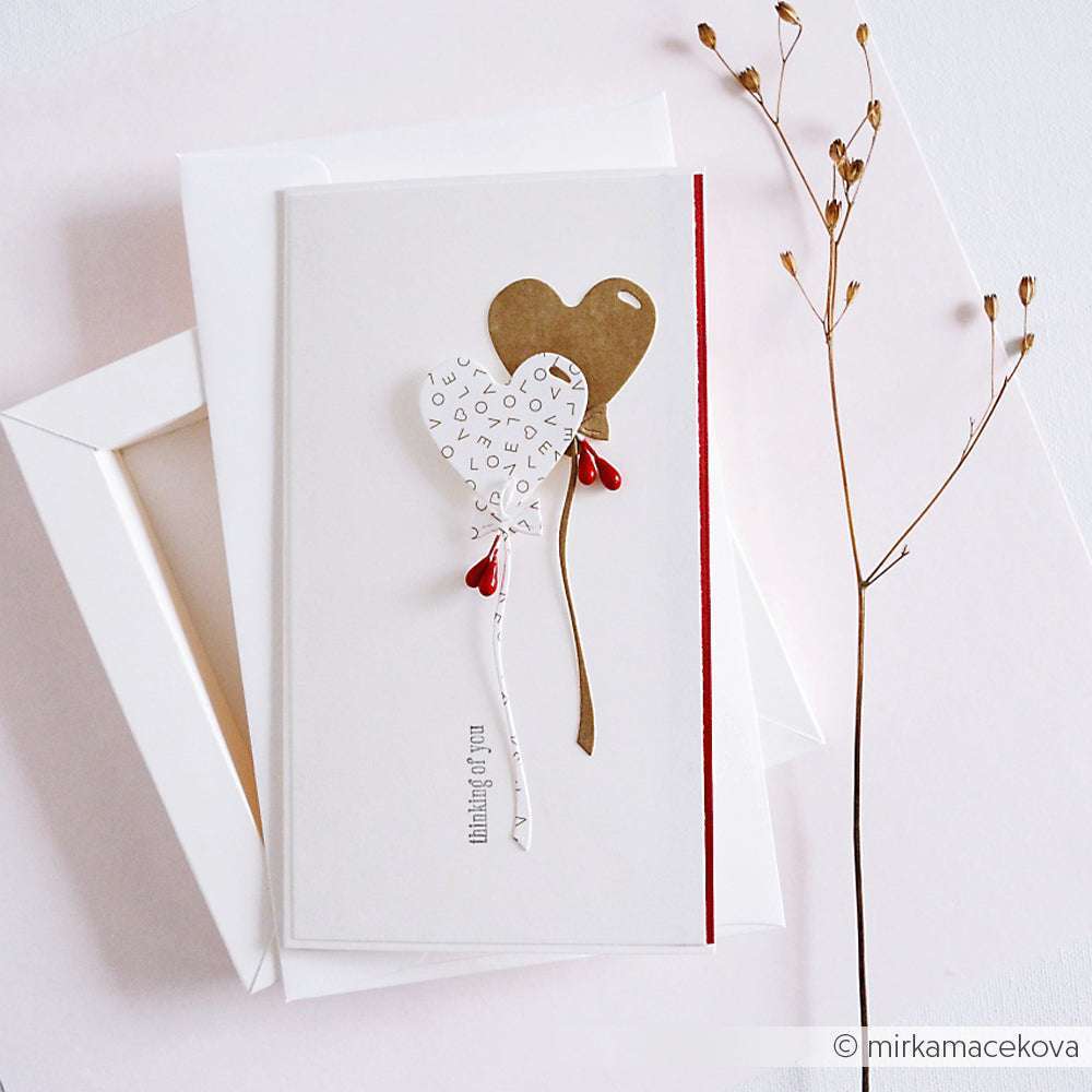 Grußkarte mit Herzballons - einer weiß mit Text, einer goldfarben - hergestellt mit Alexandra Renke DieCut Systeme und Motivstanze Herzballon Grüße, gestylt neben getrockneten Blumen auf einer weißen Fläche.