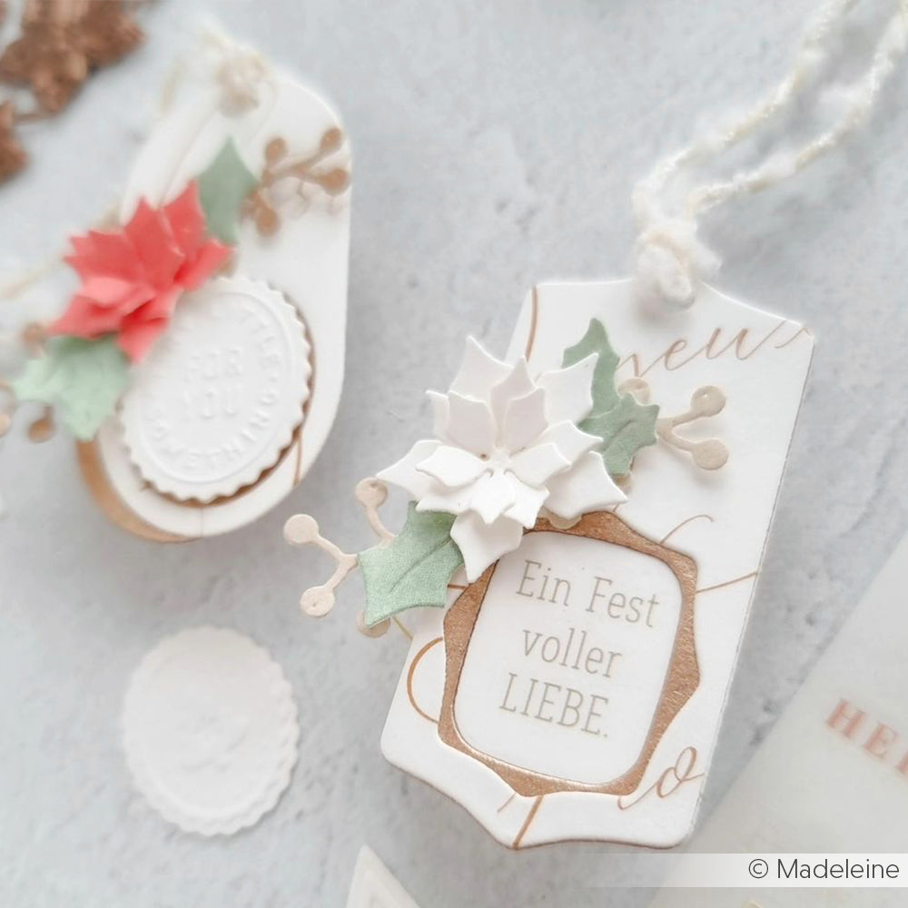 Die handgefertigten Weihnachtsgeschenkanhänger von Alexandra Renke zeigen weiße, rote und grüne Papierblumen, den deutschen Text "Ein Fest voller LIEBE" und ein geschichtetes Etikett mit Rahmen, das mit der Motivstanze gefertigt wurde und einen festlichen Touch hat.