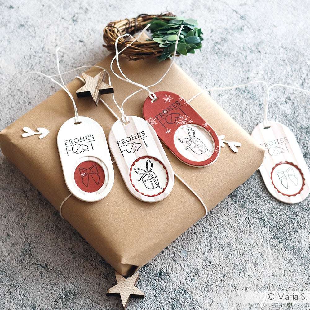 Eingepacktes Geschenk mit handgefertigten Weihnachtsanhängern, hergestellt mit Alexandra Renke Motivstanze Schichtetikett Dies und Holzsternen, dargestellt auf einer strukturierten Oberfläche.