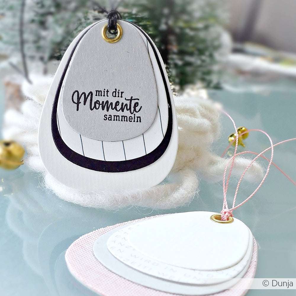 Auf den ovalen Geschenkanhängern von Alexandra Renke, die mit Motivstanze und Kombinations-Etikett hergestellt wurden, steht der Satz "Mit dir Momente sammeln", der mit einer Schnur verziert ist und vor einem festlichen Hintergrund steht.