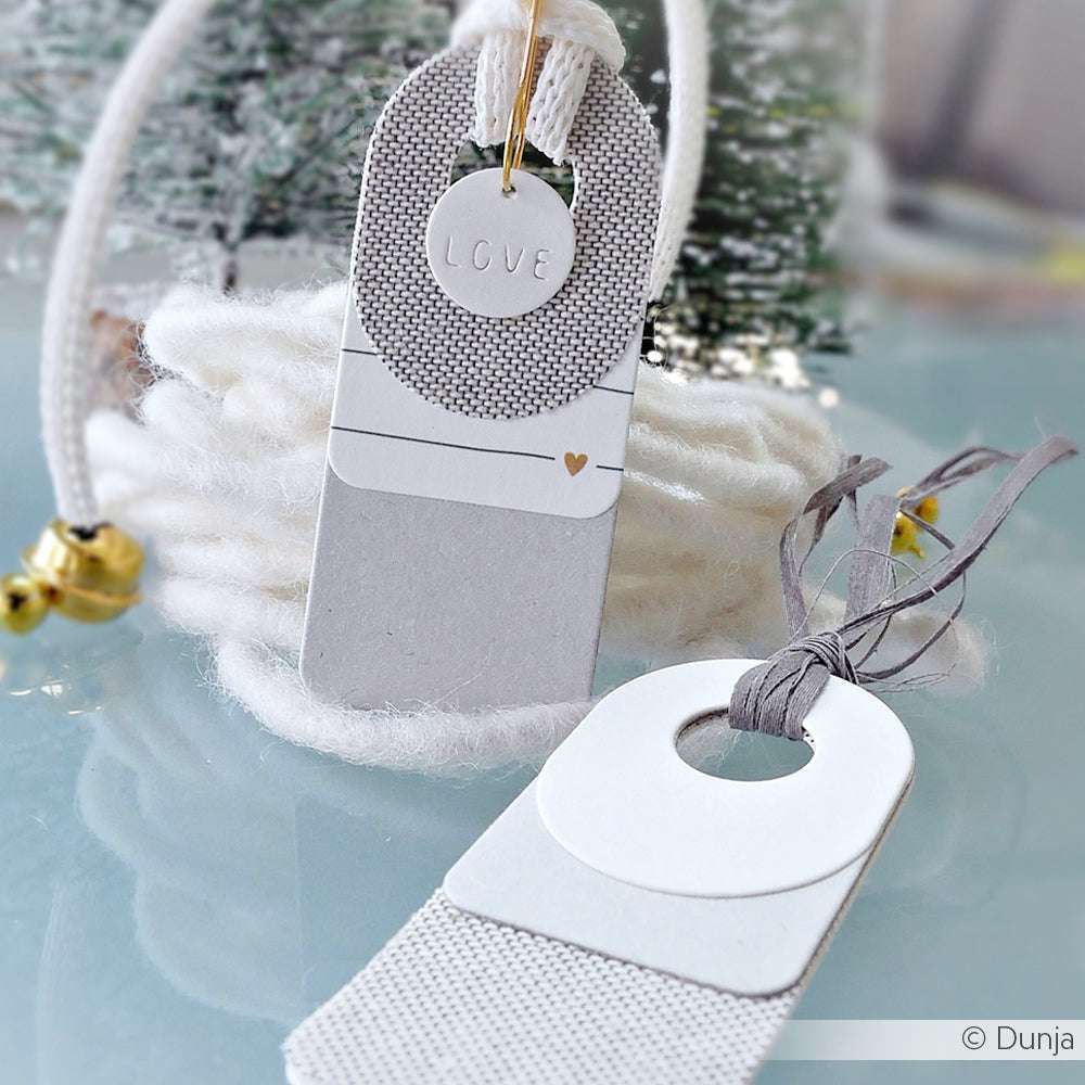Zwei moderne, handgefertigte Geschenkanhänger von Alexandra Renke mit strukturierten Details und dem Wort LOVE, gefertigt mit einer Motivstanze als stilvolles Kombinations-Etikett, ausgestellt auf einer hellen Fläche.