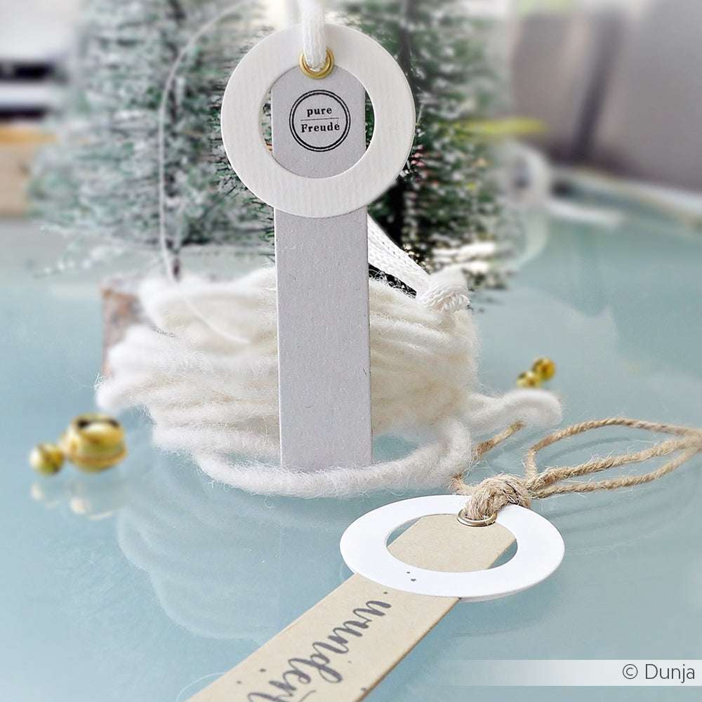 Ein handgefertigtes weißes Papierornament mit rundem Rahmen und Anhänger, hergestellt mit Alexandra Renke Stanzsysteme und Motivstanze Kombinations-Etikett, auf Glas mit Garn und Dekor.