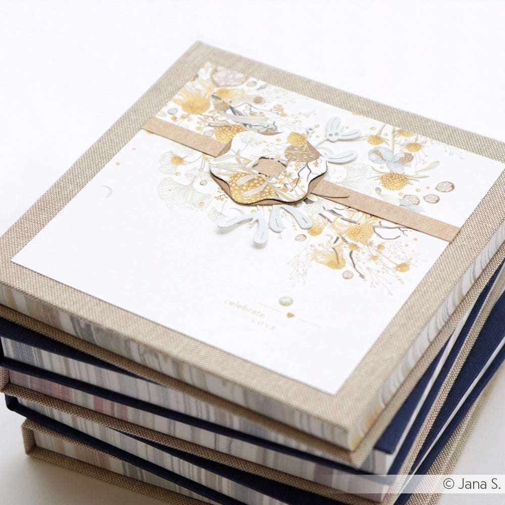 Ein Stapel dekorierter quadratischer Geschenkschachteln von Alexandra Renke, wobei die oberste Schachtel mit floralen Designpapieren und einem beigen Band verziert ist, die präzise mit DieCut Systemen gefertigt wurden.