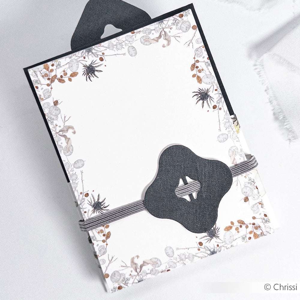 Eine Alexandra Renke-Karte mit Blumenmuster, schwarzer Zierspange und gestreiftem Band ist auf einer weißen Fläche abgebildet.