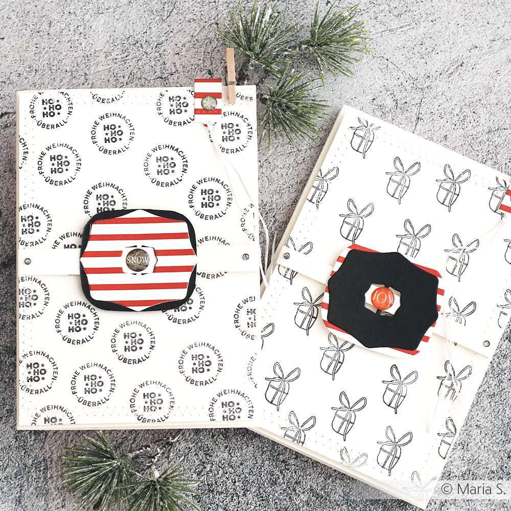 Zwei verpackte Geschenke mit festlichen Motiven in Schwarz, Weiß und Rot, hergestellt mit Alexandra Renke Motivstanze Schnallen-Kombi 4 Dies und Designpapieren, umgeben von Tannenzweigen auf einer grauen Oberfläche.