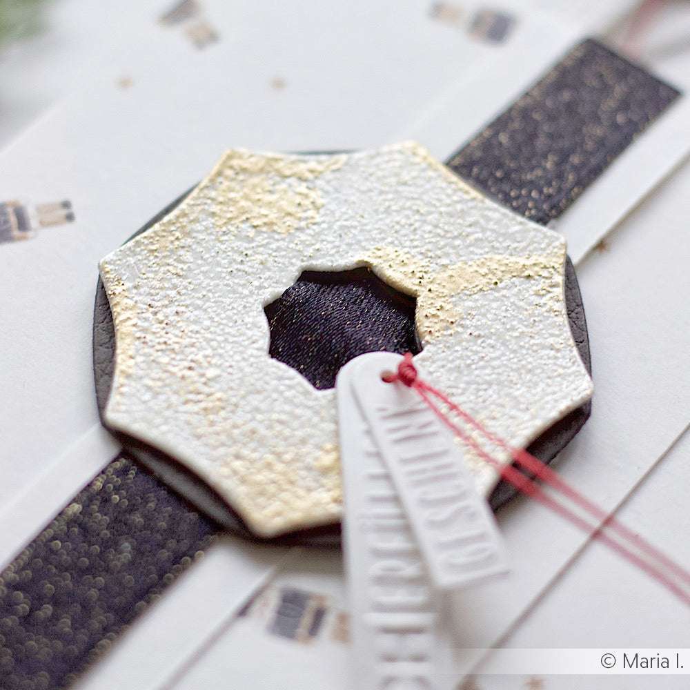 Nahaufnahme eines dekorativen, strukturierten Wachssiegels mit Sternform auf weißen Anhängern und dunklem Band - perfekt für einzigartige Akzente auf Designpapieren oder zur Verwendung mit der Motivstanze Schnallen-Kombi 5 von Alexandra Renke.