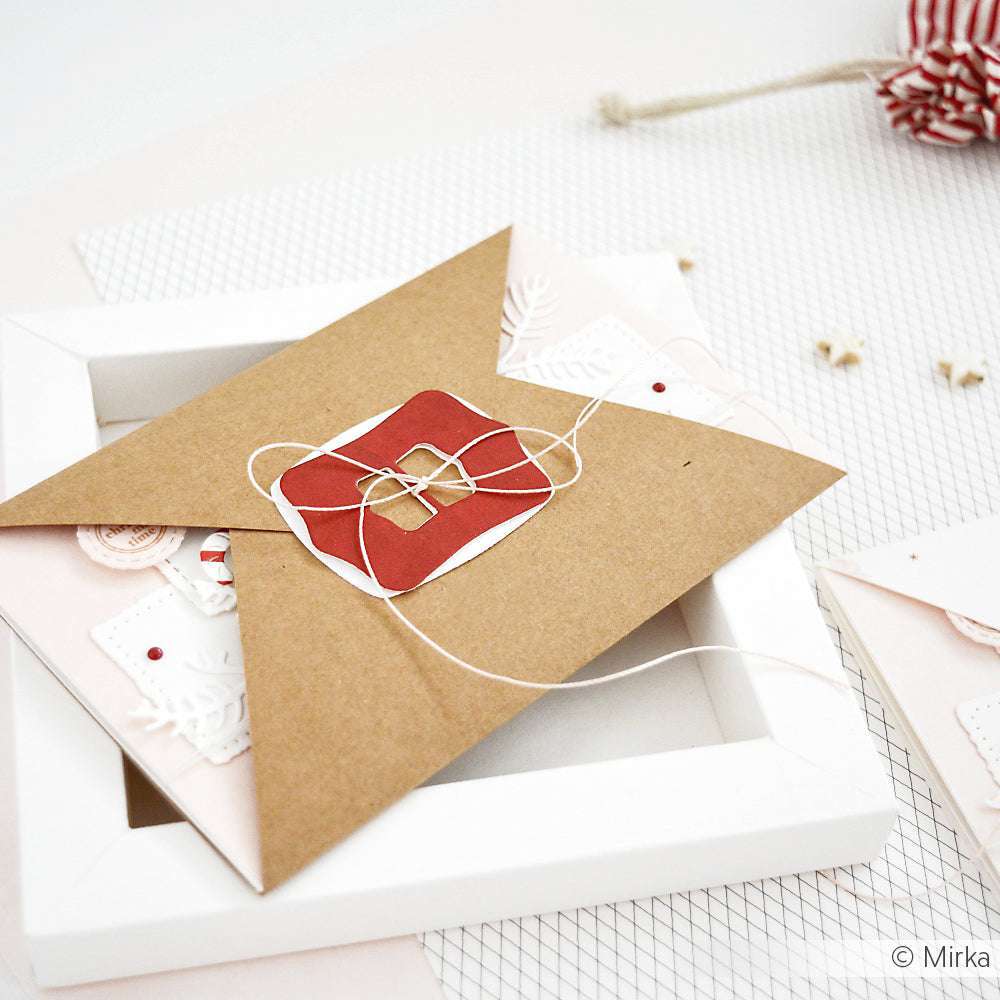 Brauner Umschlag mit Schnur gebunden, verziert mit einem roten Anhänger aus der Schnallen-Kombi 6 von Alexandra Renke, platziert auf einem weißen Rahmen vor einem weichen Hintergrund.