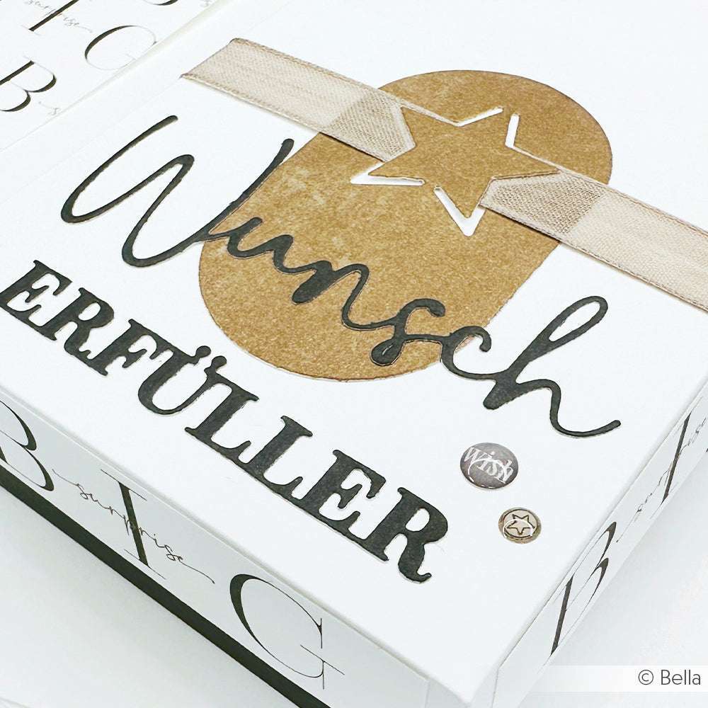 Weiße Dose von Alexandra Renke mit fettgedrucktem Schriftzug "Wunscherfüller", einem goldenen Stern aus der Motivstanze Stern-Schnalle und beigem Bandschmuck auf dem Deckel.