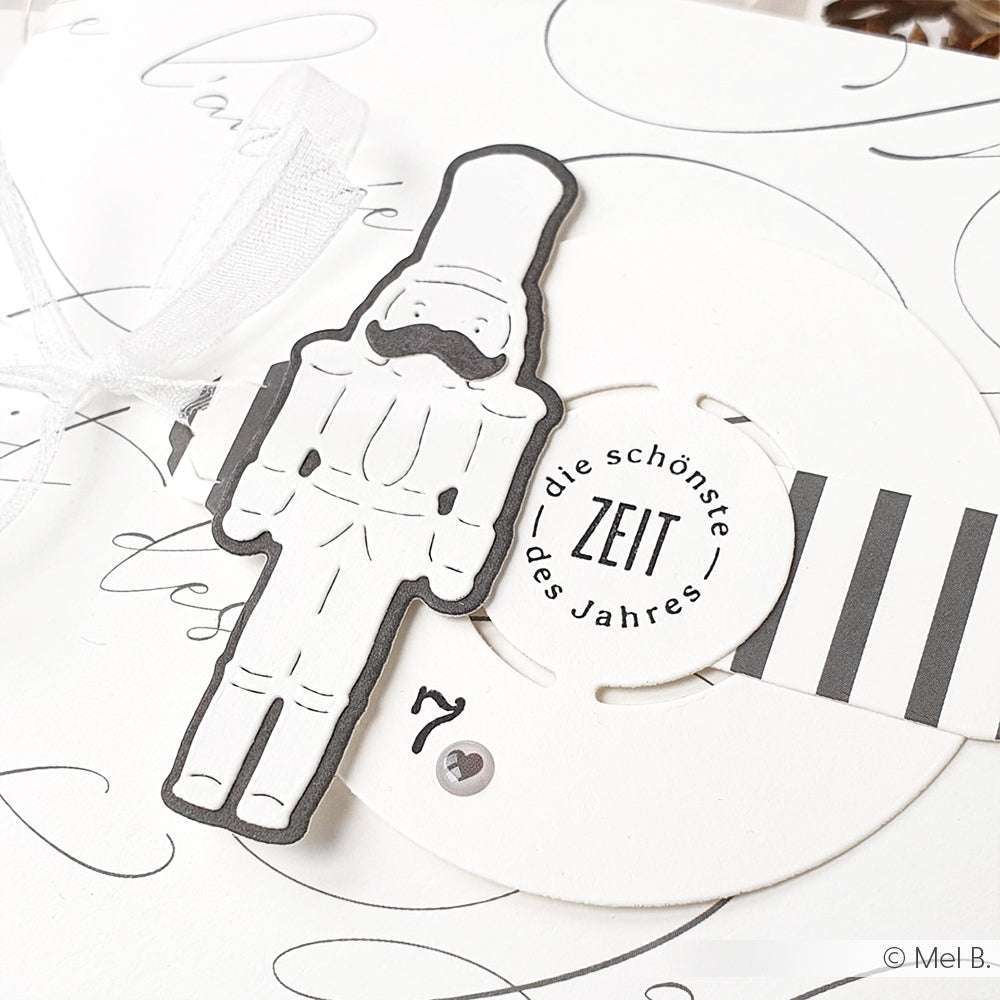 Schwarz-weiße Nussknackerdekoration auf einer festlichen Karte mit deutschem Text und Schleife, mit Alexandra Renke Designpapier und mit der Motivstanze Kreis-Schnalle Stanzsysteme verschönert.