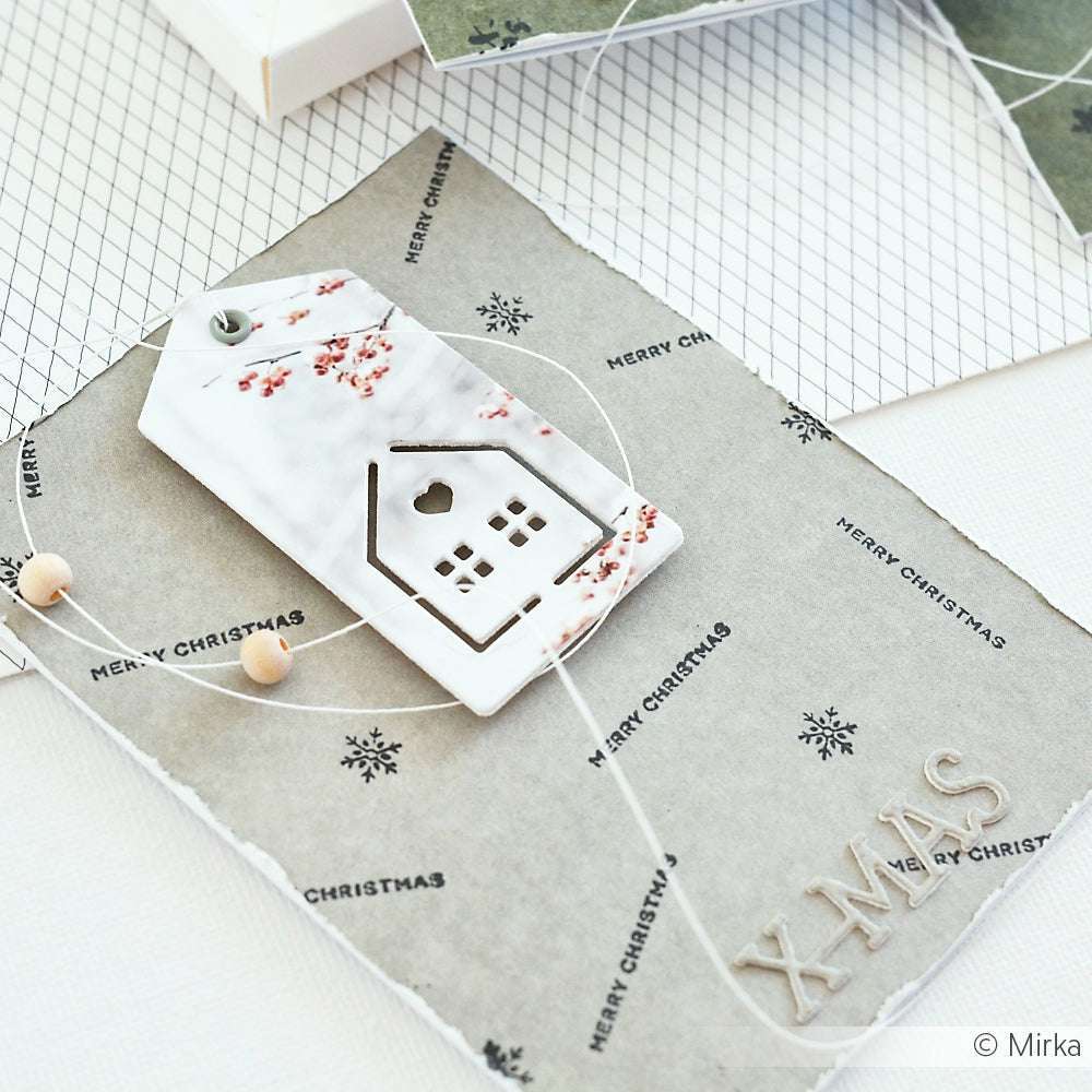 Handgefertigte Weihnachtskarte auf Alexandra Renke-Papier mit einem Hausanhänger aus Keramik in Form der Motivstanze Haus-Schnalle, sowie Perlen und XMAS-Buchstaben für einen festlichen Touch.