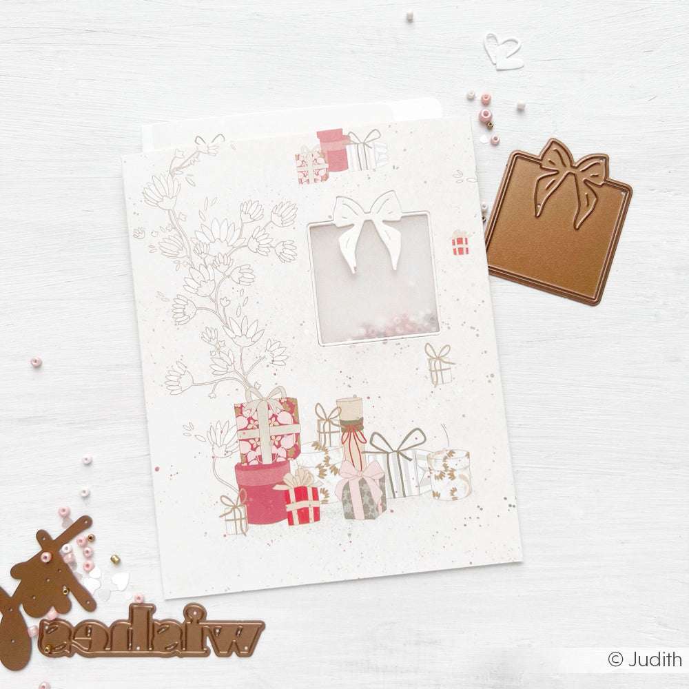 Eine festliche Karte von Alexandra Renke, die mit Geschenkillustrationen, einem Fensterausschnitt und Bastelmaterial wie DieCut Systemen und Designpapieren auf einer weißen Fläche verziert ist.