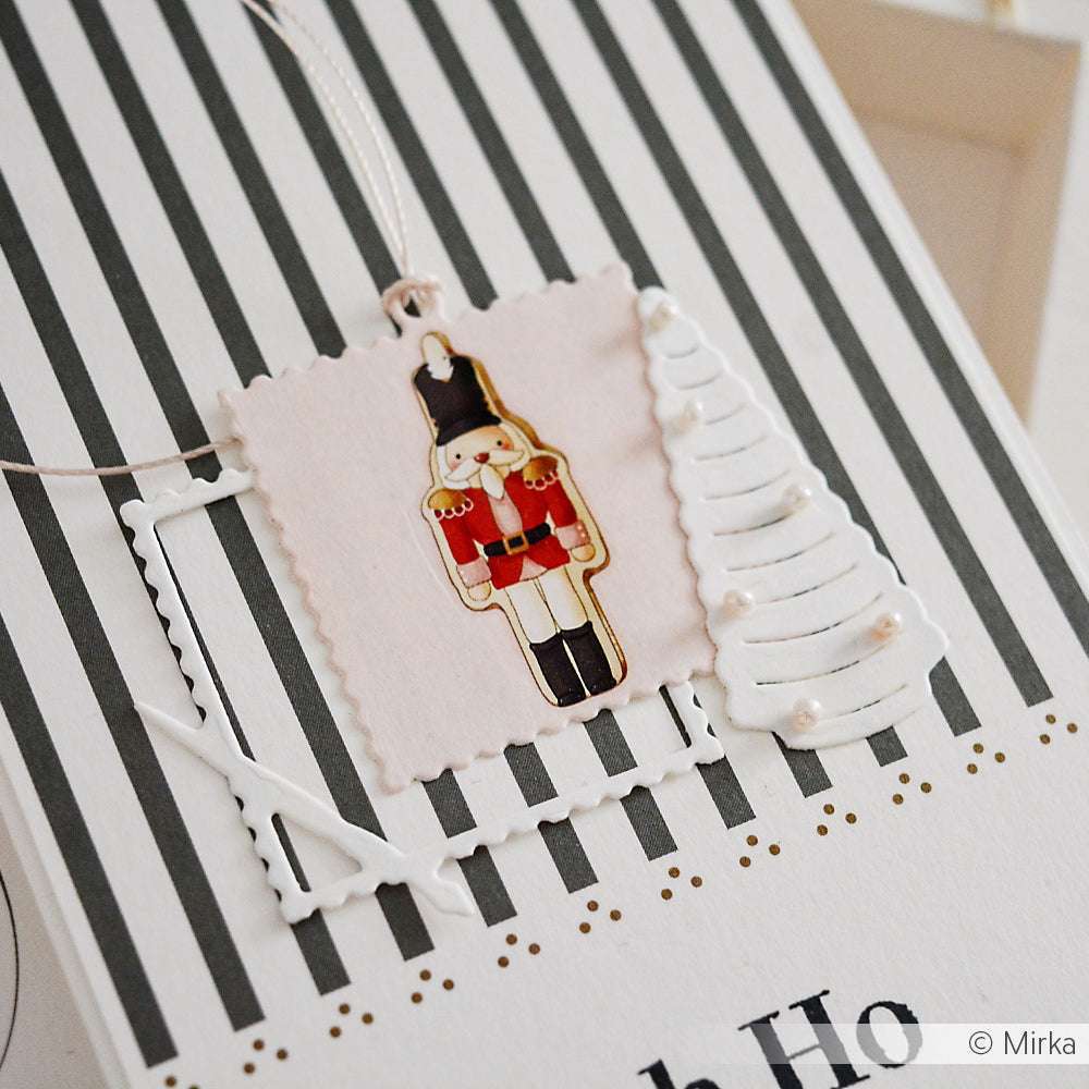 Handgefertigte Weihnachtskarte von Alexandra Renke mit einer Nussknacker-Illustration, weißem Baumschmuck und gestreiftem Hintergrund, akzentuiert mit einer Motivstanze Briefmarken-Rahmen, die für einen eleganten Touch sorgt.