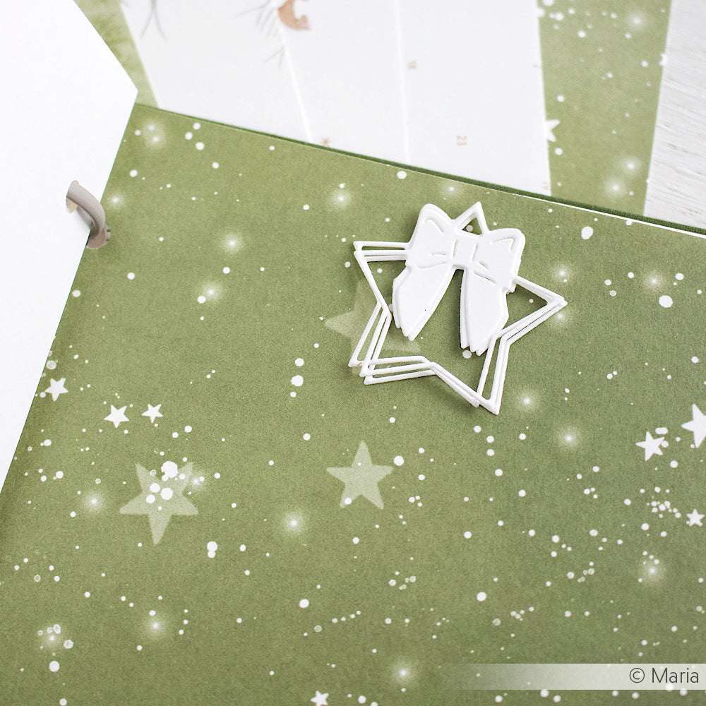 Weiße Büroklammer in Form von Ballettschuhen auf grünem Sternenhintergrund, hergestellt mit Alexandra Renke Motivstanze Stern, mit weißen und beigen Alexandra Renke Designpapieren daneben.