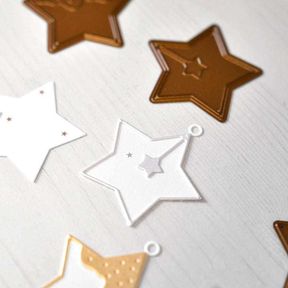 Sternförmige Papier- und Metallausschnitte, die mit Alexandra Renke Motivstanze Stern hergestellt wurden, sind auf einer hellen Holzoberfläche angeordnet.