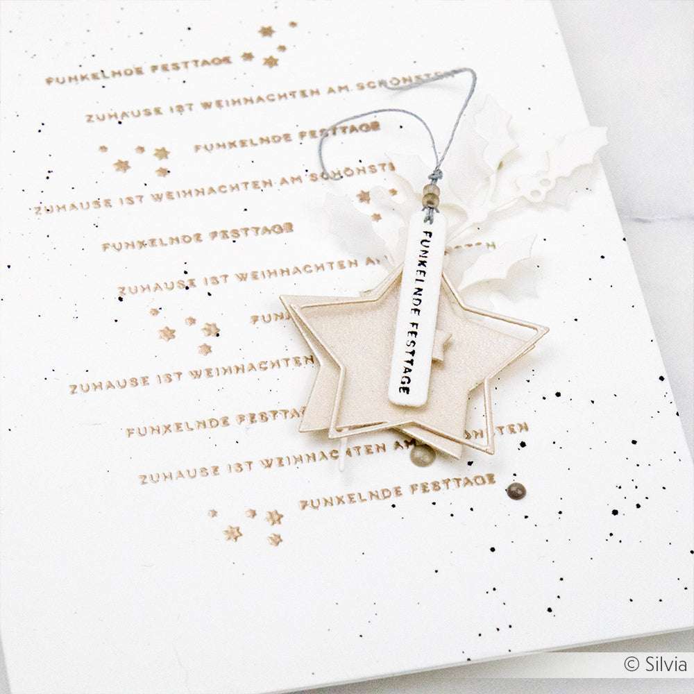 Weiße Karte mit goldenen Sternen und deutschem Text, mit geschichteten Sternornamenten, die mit Alexandra Renke Motivstanze Stern im Stern Dies hergestellt wurden, verziert mit einem Funkelnde Festtage Anhänger.