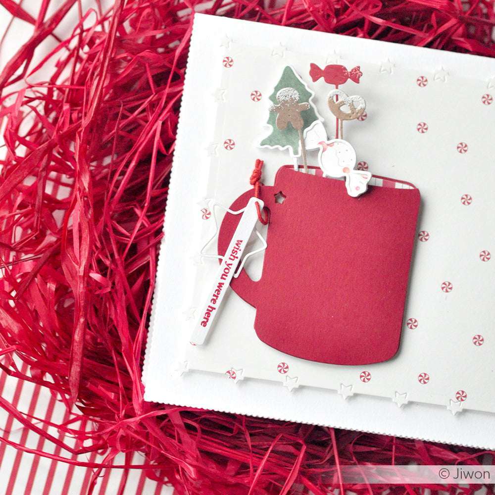 Die festliche Karte von Alexandra Renke zeigt eine rote Tasse, eine Zuckerstange, einen Baum und einen Schneemann auf weißem Papier mit roten Raspelakzenten - perfekt für Ihre DieCut Systeme oder Motivstanze Sternrand Kartenaufleger.