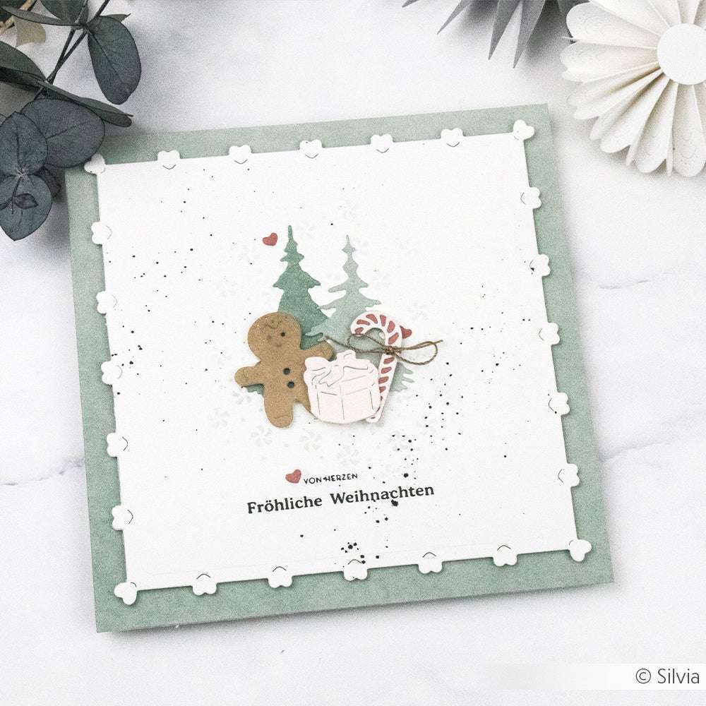 Handgemachte Weihnachtskarte von Alexandra Renke mit Designpapier und DieCut-System. Mit Lebkuchenmann, Geschenk, Zuckerstange, Bäumen und "Fröhliche Weihnachten" auf einem Herzrand-Kartenaufleger.