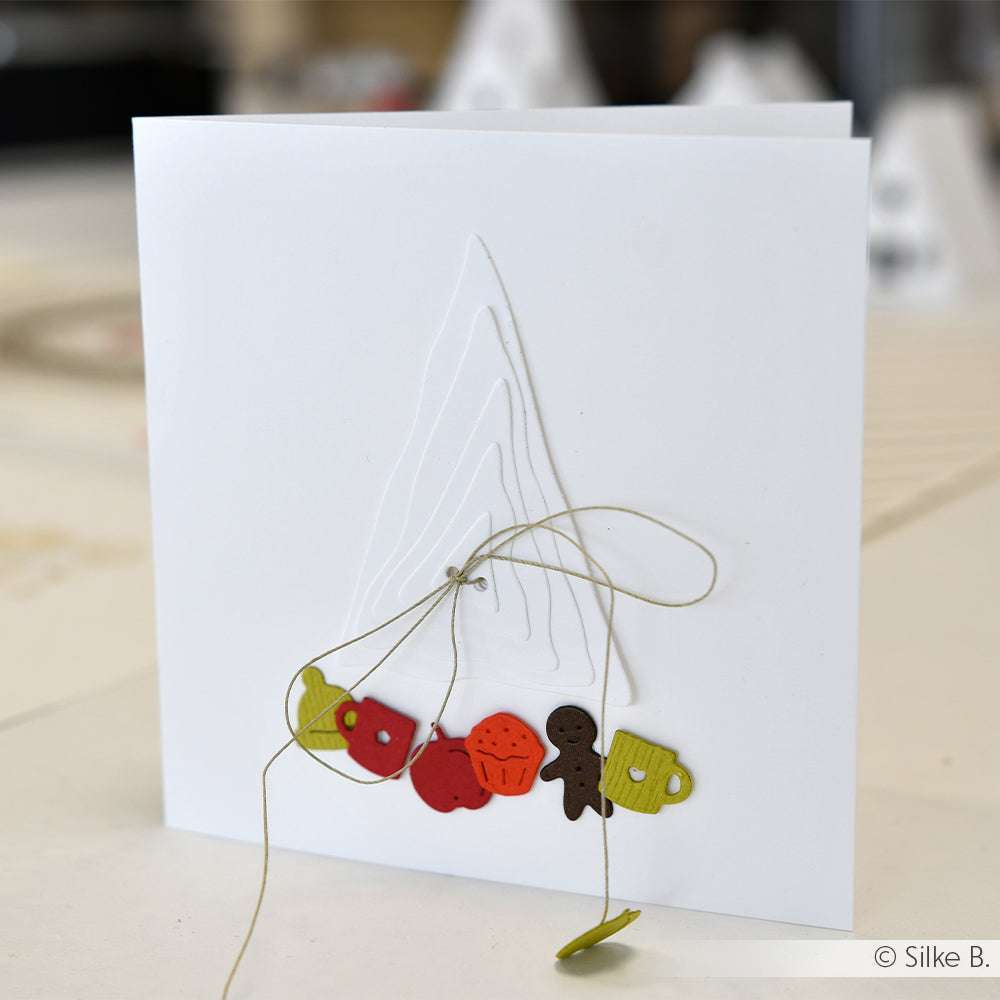 Die quadratische weiße Karte von Alexandra Renke, die mit Designpapier gestaltet wurde, zeigt einen gestickten Baumumriss und bunte Weihnachtsformen am Boden, die mit DieCut Systemen hergestellt wurden.