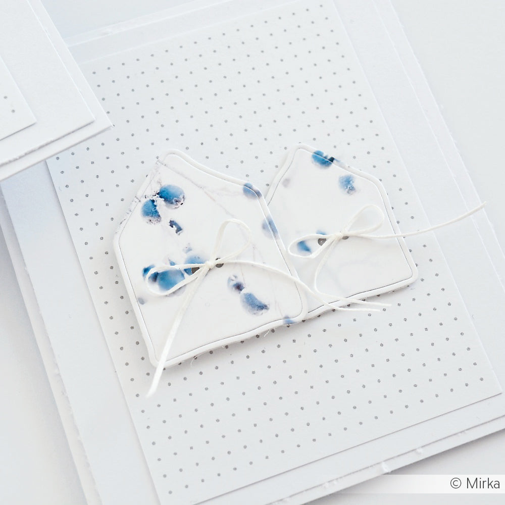 Zwei weiße, hausförmige Ausschnitte von Alexandra Renke mit blauen Punkten sind mit weißer Schnur zusammengebunden und stehen auf einem gepunkteten weißen Hintergrund.