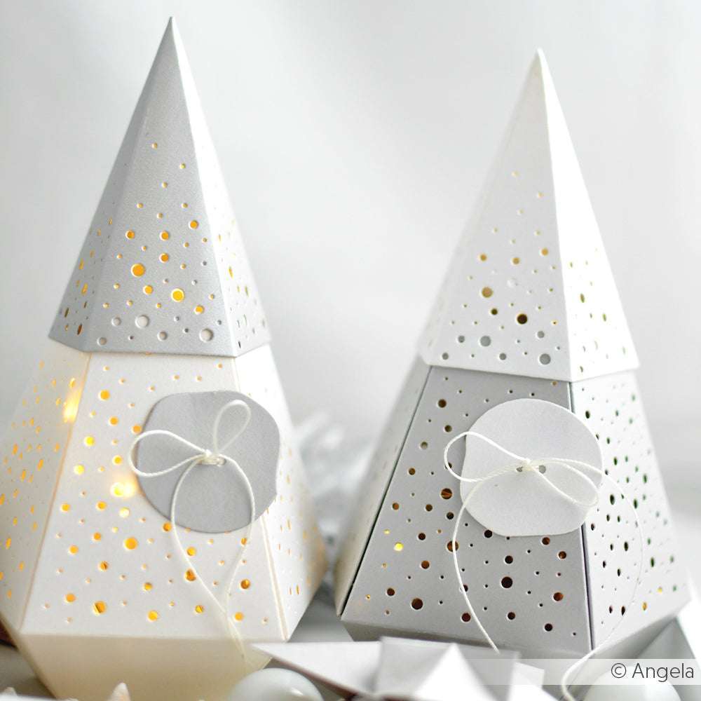 Zwei weiße, kegelförmige Papierlaternen von Alexandra Renke sind aus Designpapier mit kleinen Stanzlöchern gefertigt und mit dekorativen Schnurschleifen an der Vorderseite versehen.