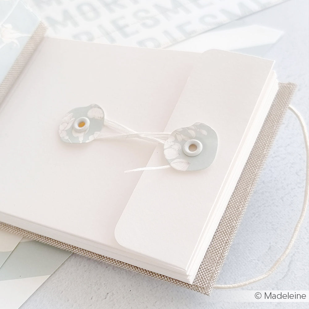 Eine Nahaufnahme eines aufgeschlagenen Notizbuchs mit einem Umschlag mit Kordelzug und wunderschön gestalteten Alexandra Renke Designpapieren auf einer leicht strukturierten Oberfläche.