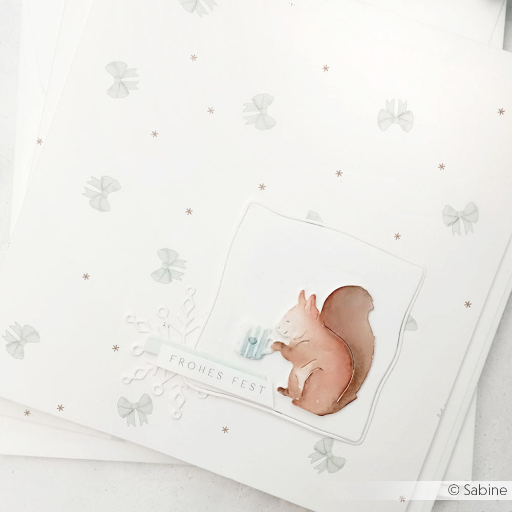 Weiße Karte von Alexandra Renke mit einem Eichhörnchen, einer Schneeflocke und dem Schriftzug Frohes Fest" in zarten Pastelltönen - gestaltet mit Designpapieren für einen bezaubernden weihnachtlichen Look.