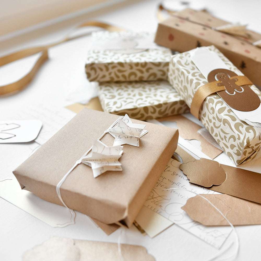 Verschiedene Geschenke, verpackt in neutrales, gemustertes Papier mit Bändern und Anhängern - einige mit Alexandra Renke Stern Etikett - sind auf einer weißen Fläche angeordnet.