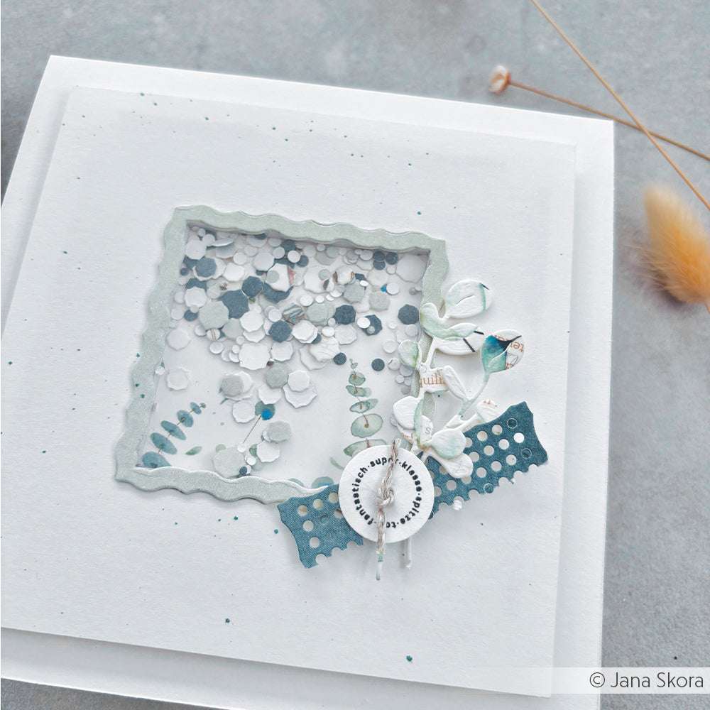 Die handgefertigte weiße Grußkarte von Alexandra Renke zeigt Konfetti in einem Fenster, blaue Blumenakzente und elegante Details, die mit Motivstanze und PAPPcut®ies auf grauem Hintergrund gestaltet wurden.