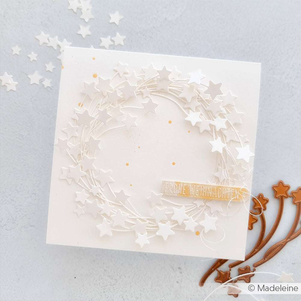 Weiße Karte mit einem Kranz aus Papiersternen, gestaltet mit Alexandra Renke Motivstanze Sternchen Zweige Trio und hochwertigen Designpapieren, veredelt mit einem kleinen "Frohe Weihnachten"-Banner auf hellem Hintergrund.