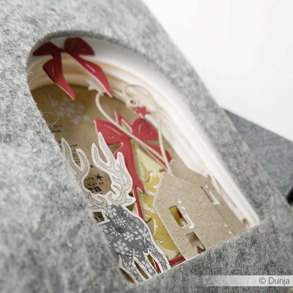 Ein Lagenpapier-Diorama von Alexandra Renke zeigt ein Reh, ein Haus und eine rote Schleife, die durch ein graues Bogenfenster zu sehen ist - gestaltet mit Designpapieren und dem Motivstanze Herzchen Häuschen DieCut System.