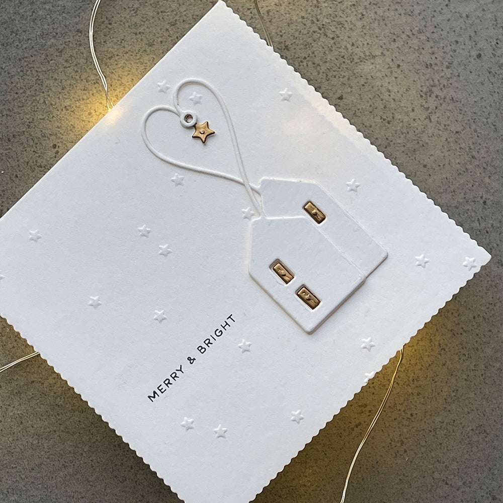 Weiße Weihnachtskarte mit einem geprägten Haus, einem goldenen Stern und "MERRY & BRIGHT" auf grauem Grund - ideal für die Motive Stanzen für Papier und Motivstanze Herzchen Häuschen von Alexandra Renke.