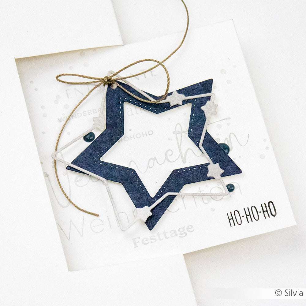 Eine handgefertigte Weihnachtskarte von Alexandra Renke mit einem blauen Sternenornament, das mit dem Motivstanze Sternenzauber und dem Text HO-HO-HO ausgeschnitten und mit Schnur gebunden wurde.