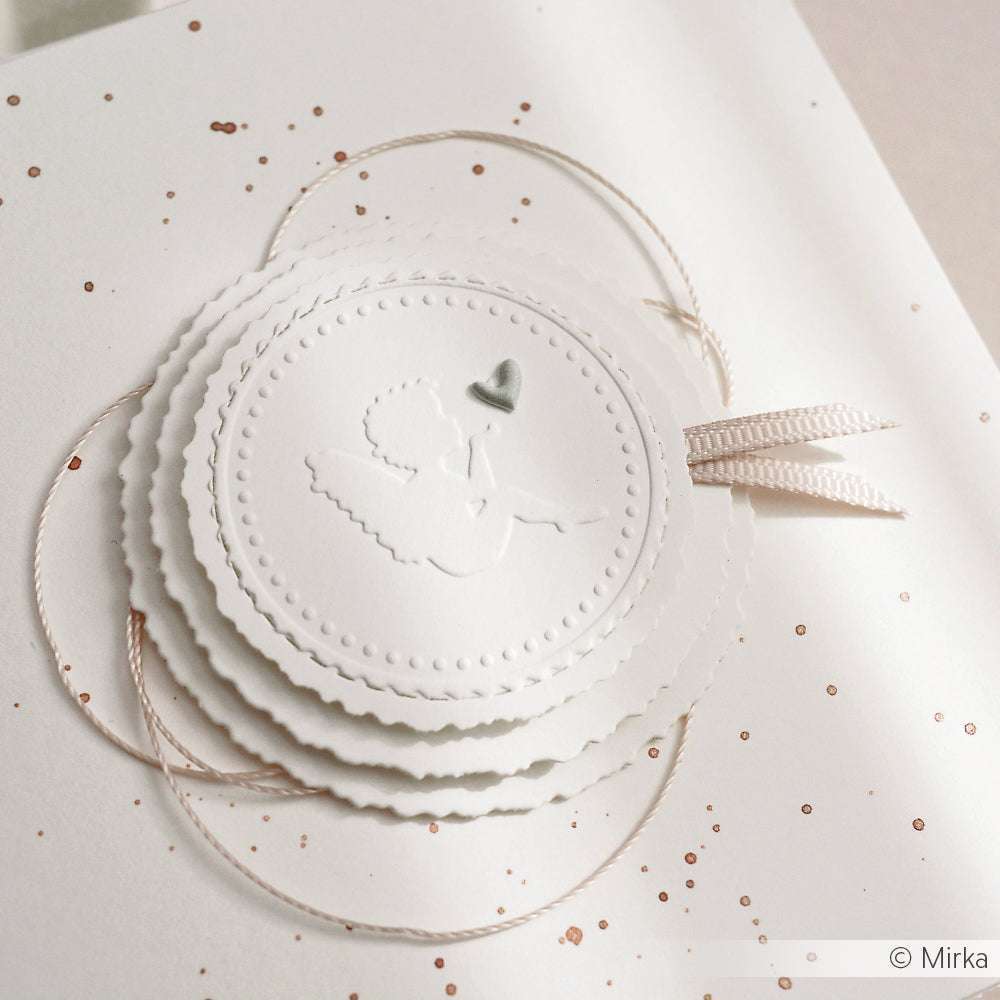 Weiße, geprägte Karte mit einem Engelchen, einem silbernen Herz und übereinander liegenden Kreisen, die mit der Alexandra Renke Motivstanze hergestellt wurden. Die Karte ist mit Schleife, Glitter und Runden Schicht-Etiketten verziert, die für ein elegantes Finish sorgen.